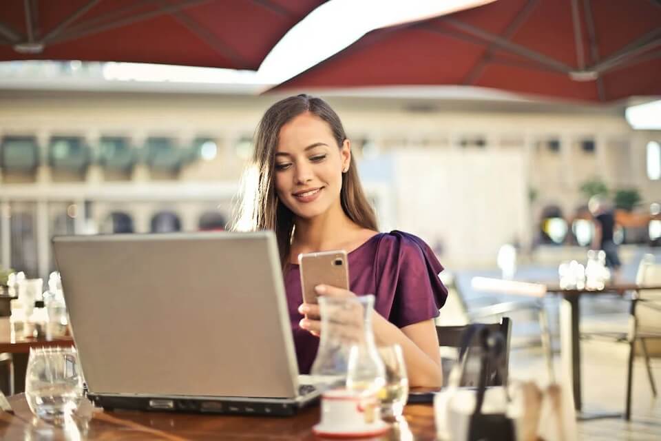 woman in front of laptop, looking at mobile phone